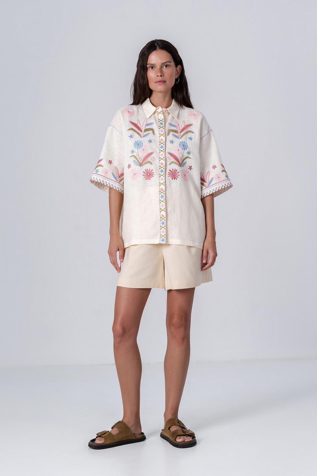 Woman wearing a white embroidered blouse and beige shorts on a white background