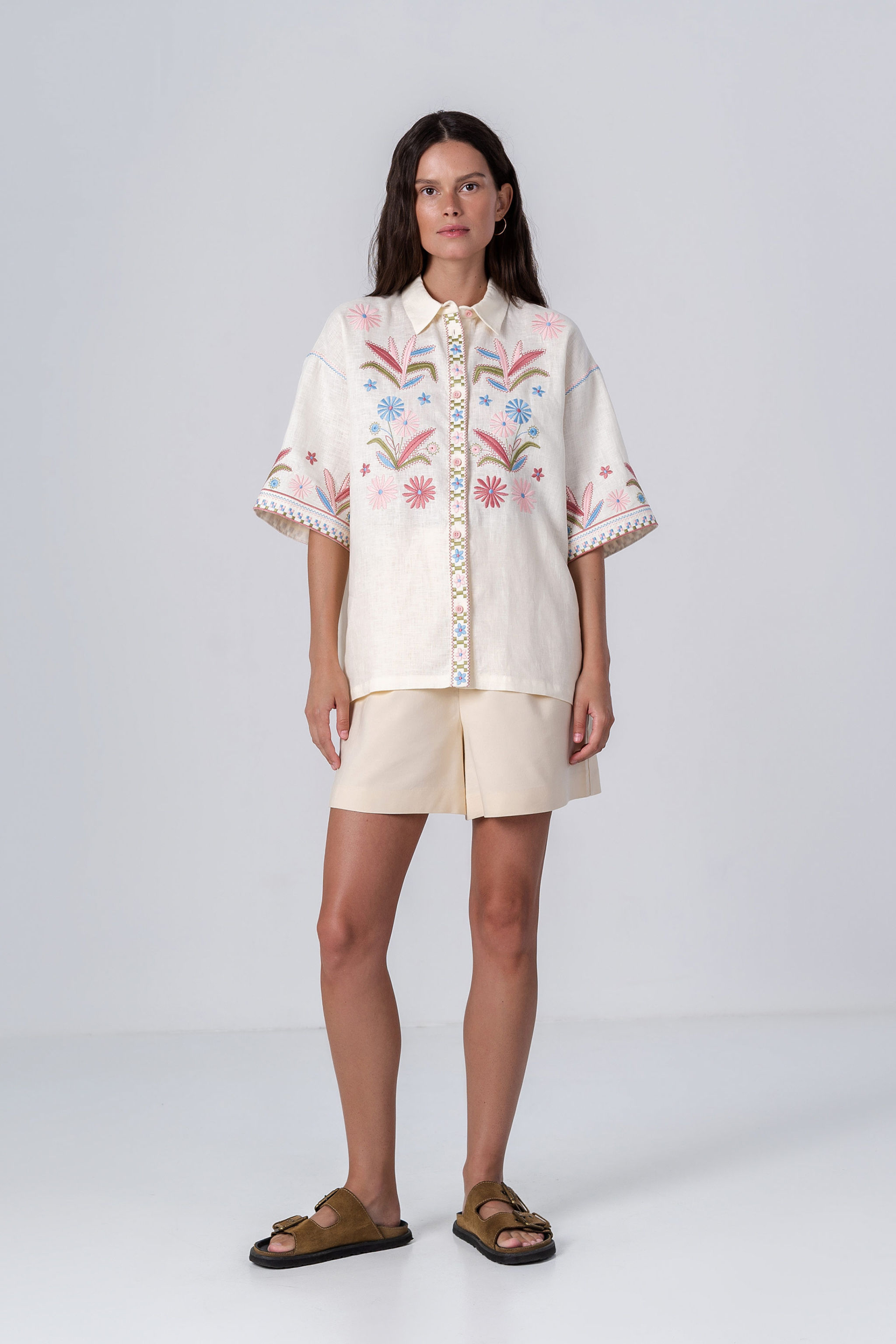 Woman wearing a white embroidered blouse and beige shorts on a white background