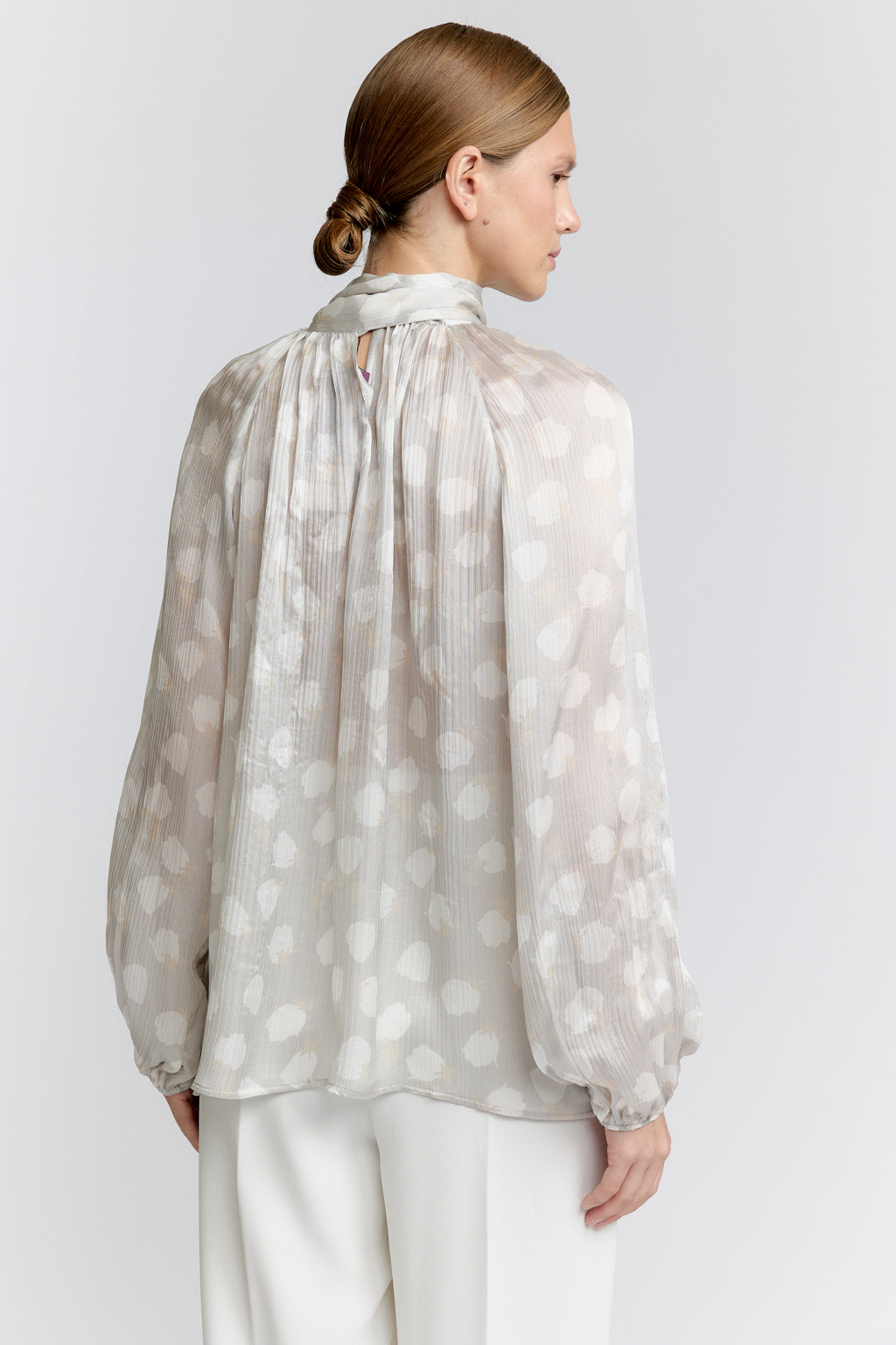 Woman wearing a light-colored blouse with a subtle pattern on a plain background