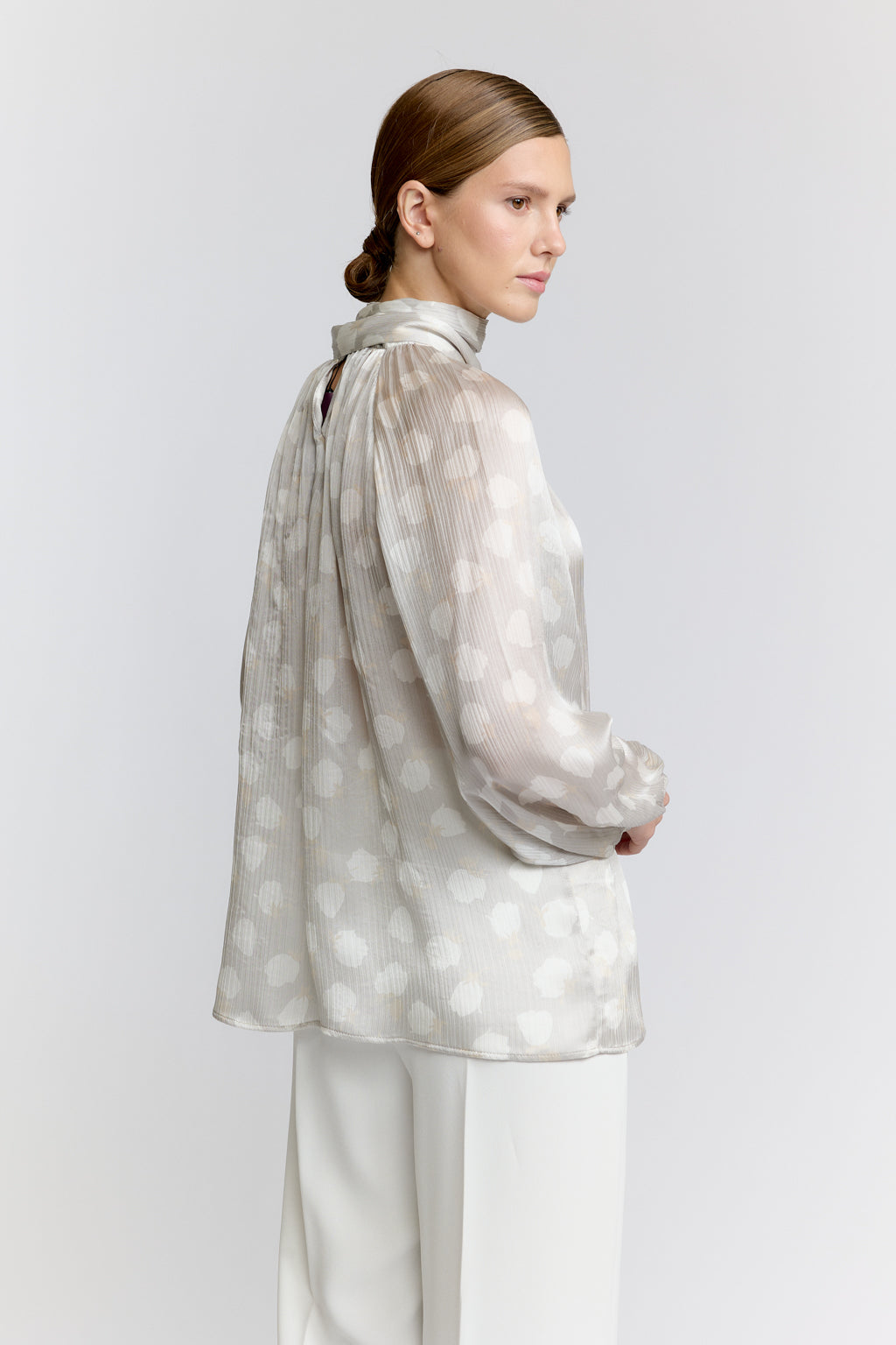 Woman wearing a light-colored polka dot blouse with a plain background