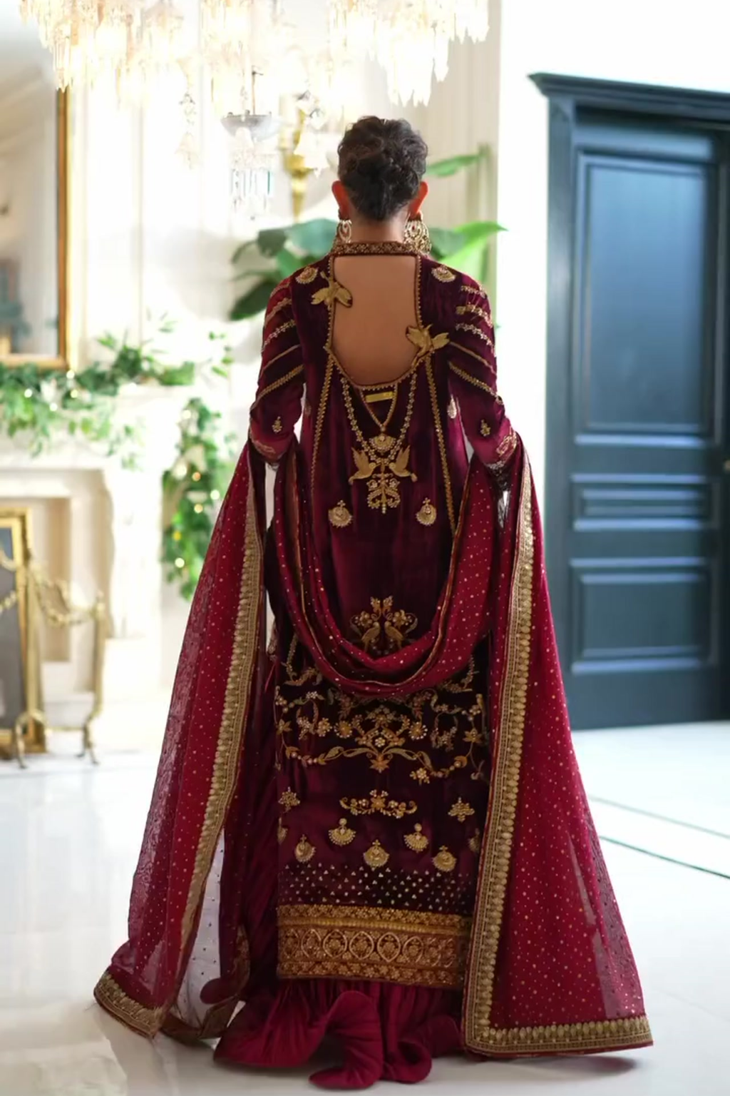 Person wearing a burgundy and gold embroidered traditional outfit in an indoor setting.