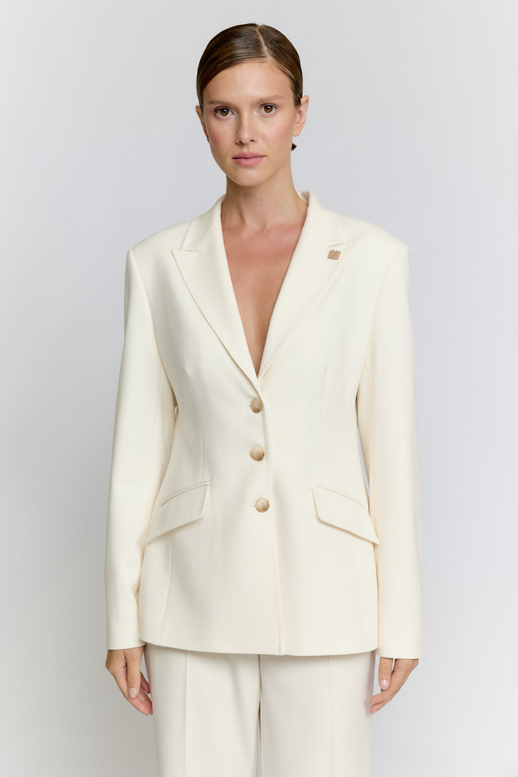Woman wearing a cream-colored suit with a plain background