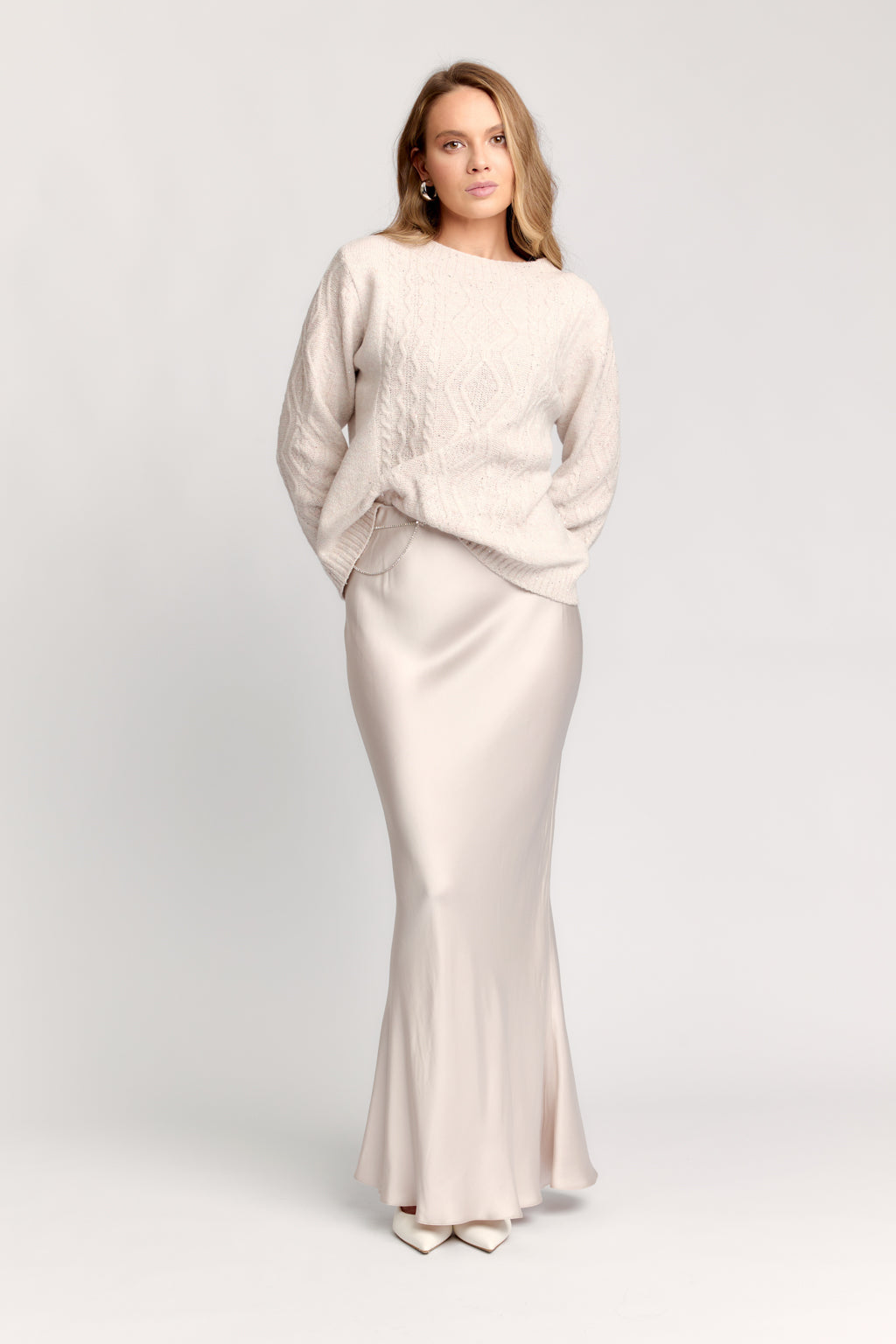 Woman wearing a light-colored sweater and skirt set on a white background