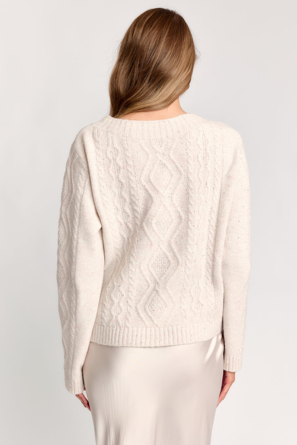 Woman wearing a cream cable knit sweater against a white background