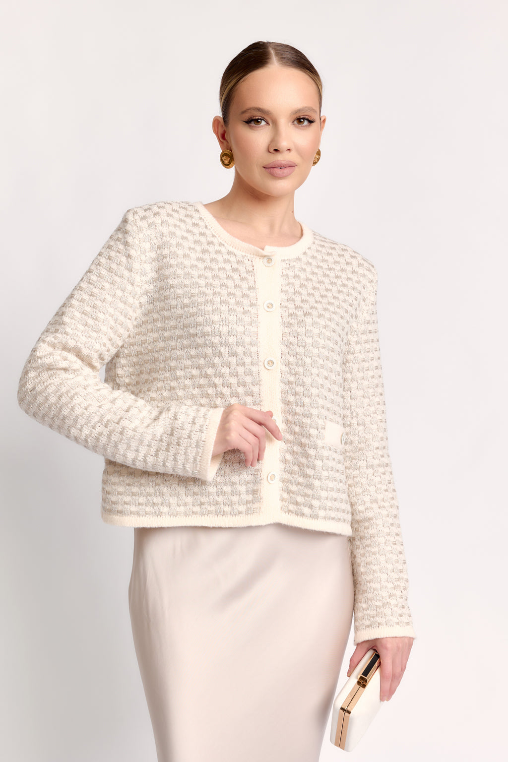 Woman wearing a textured white jacket and skirt set on a plain background