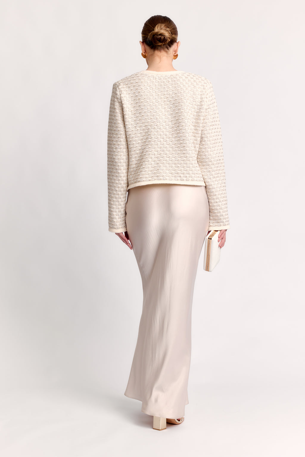 Woman wearing a textured white top and light-colored pants on a plain background