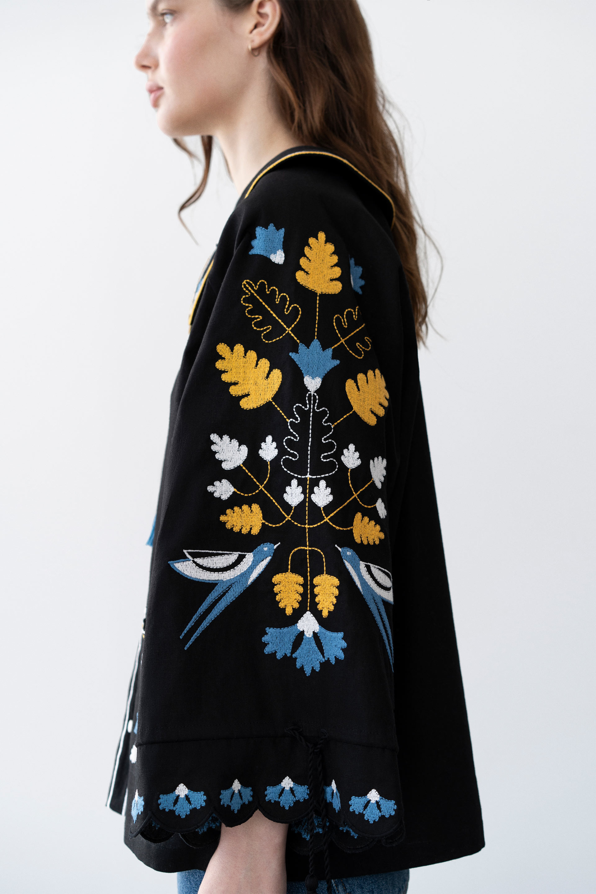 Woman wearing a black embroidered jacket with blue and yellow floral patterns on a white background
