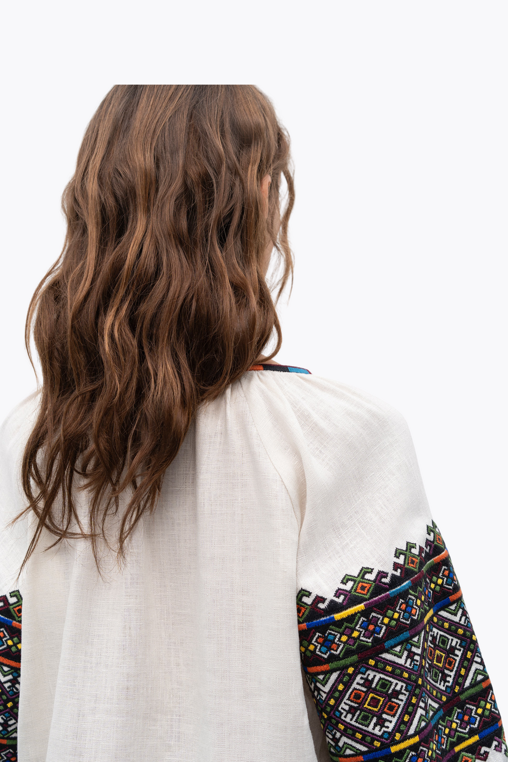 Person wearing a white garment with colorful geometric patterns on a plain background