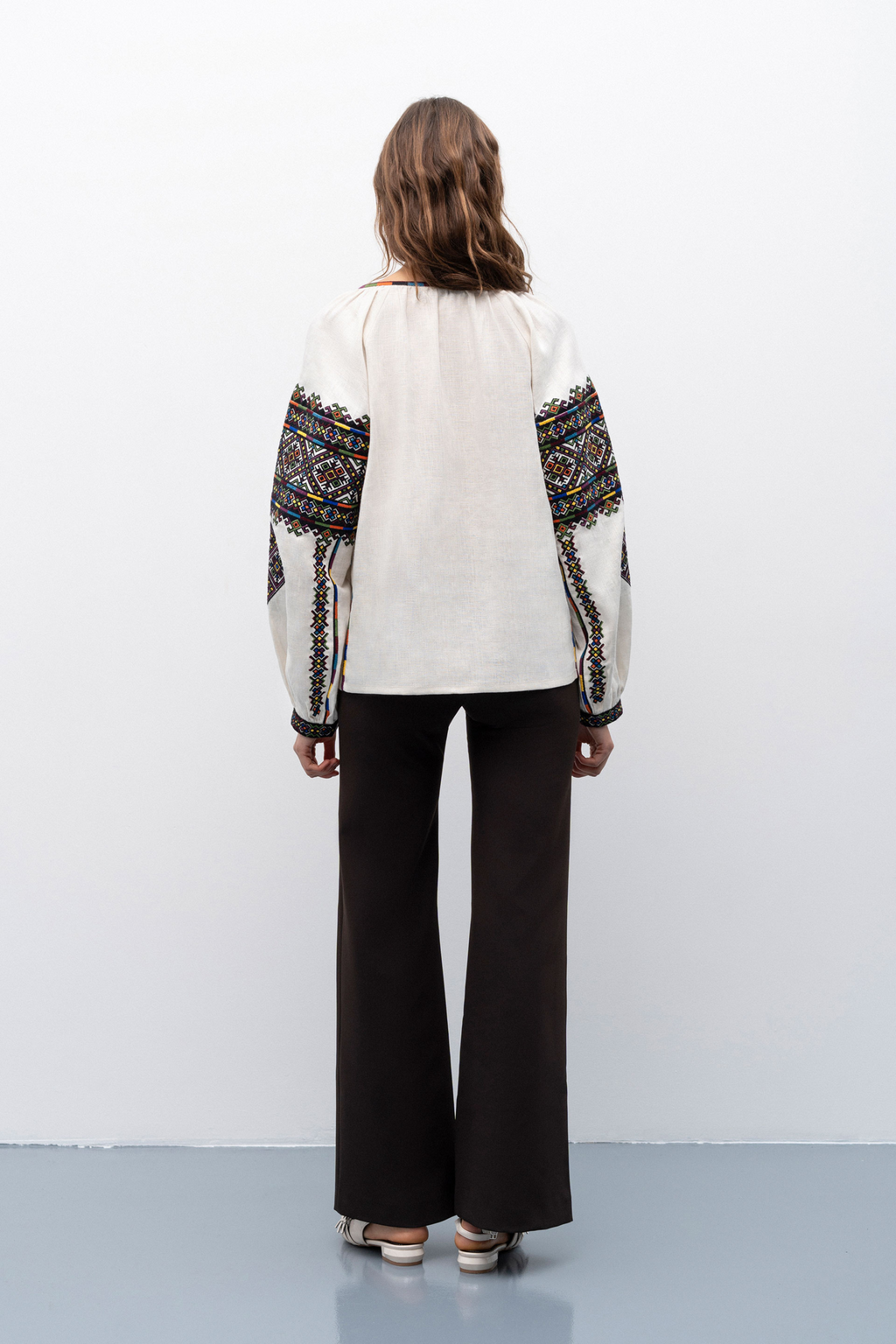 Person wearing a white blouse with black and gold embroidery and black pants on a white background