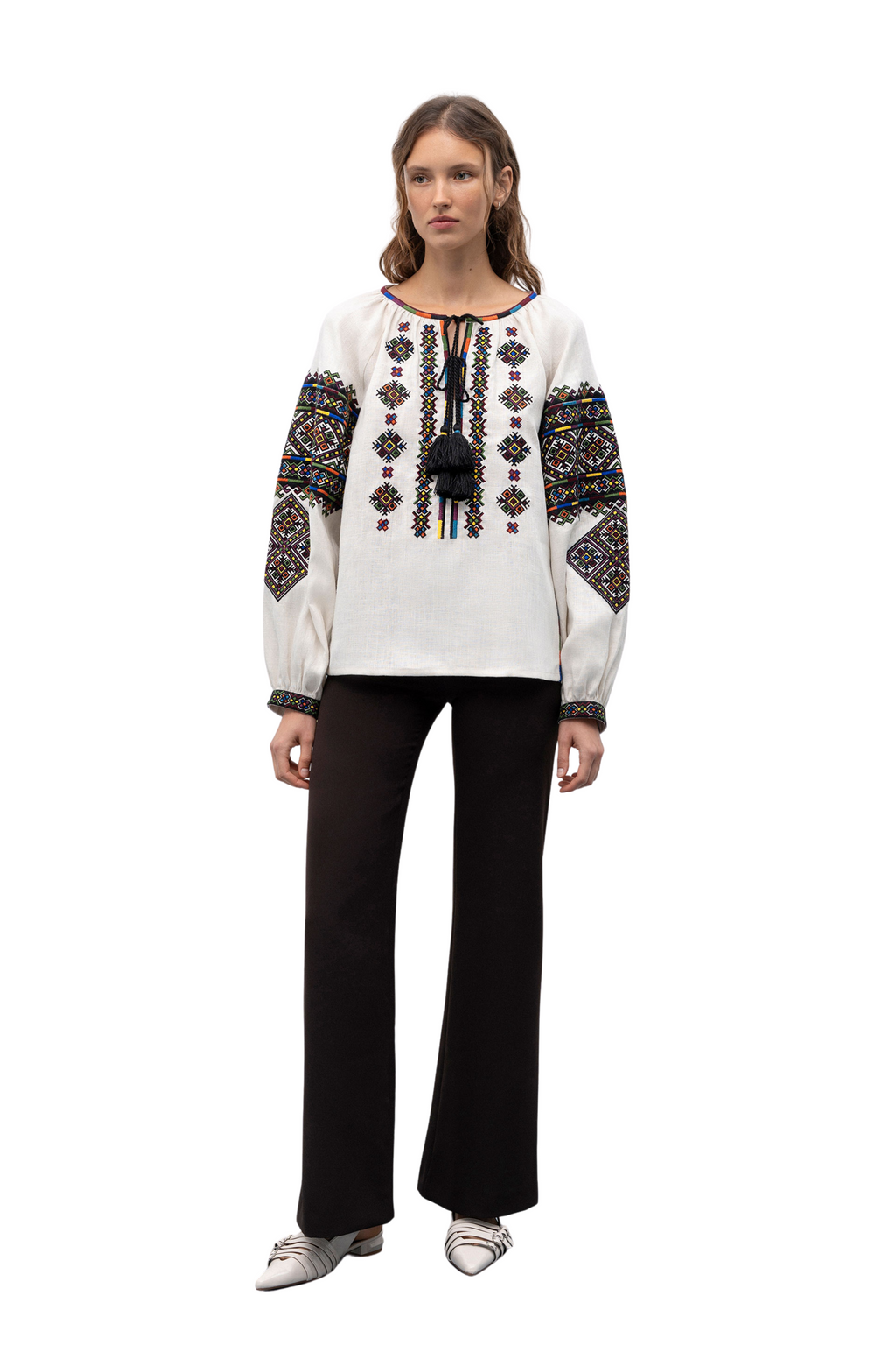 Woman wearing a white blouse with black and gold embroidery on a white background