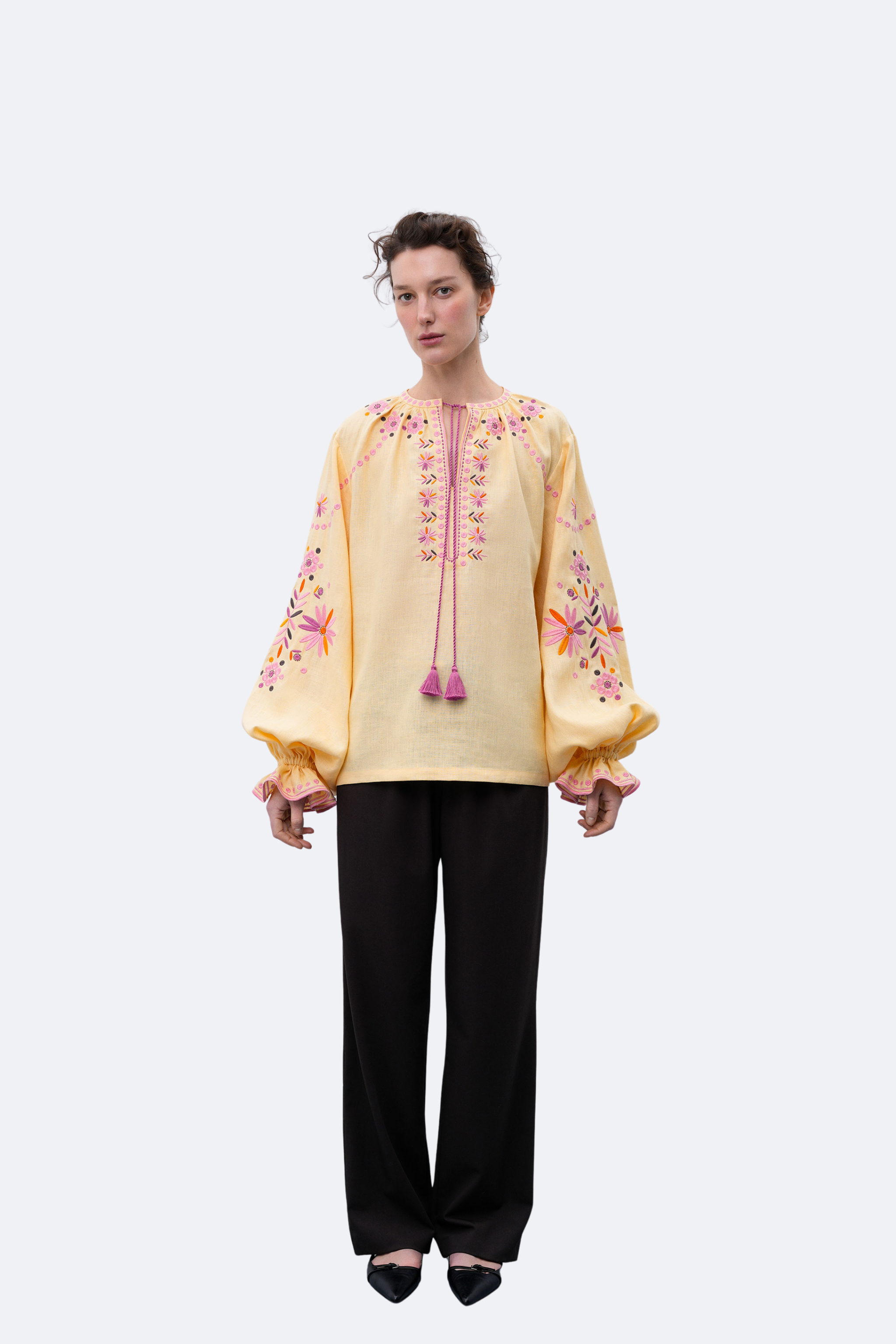 Woman wearing a yellow embroidered blouse with black pants on a white background