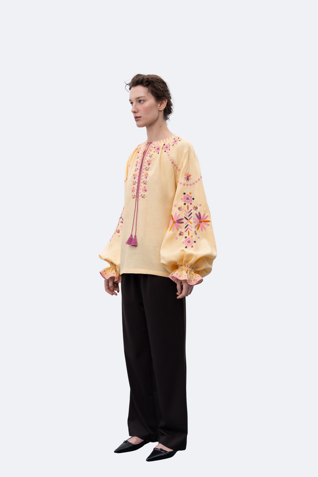 Woman wearing a yellow embroidered blouse and black pants on a white background