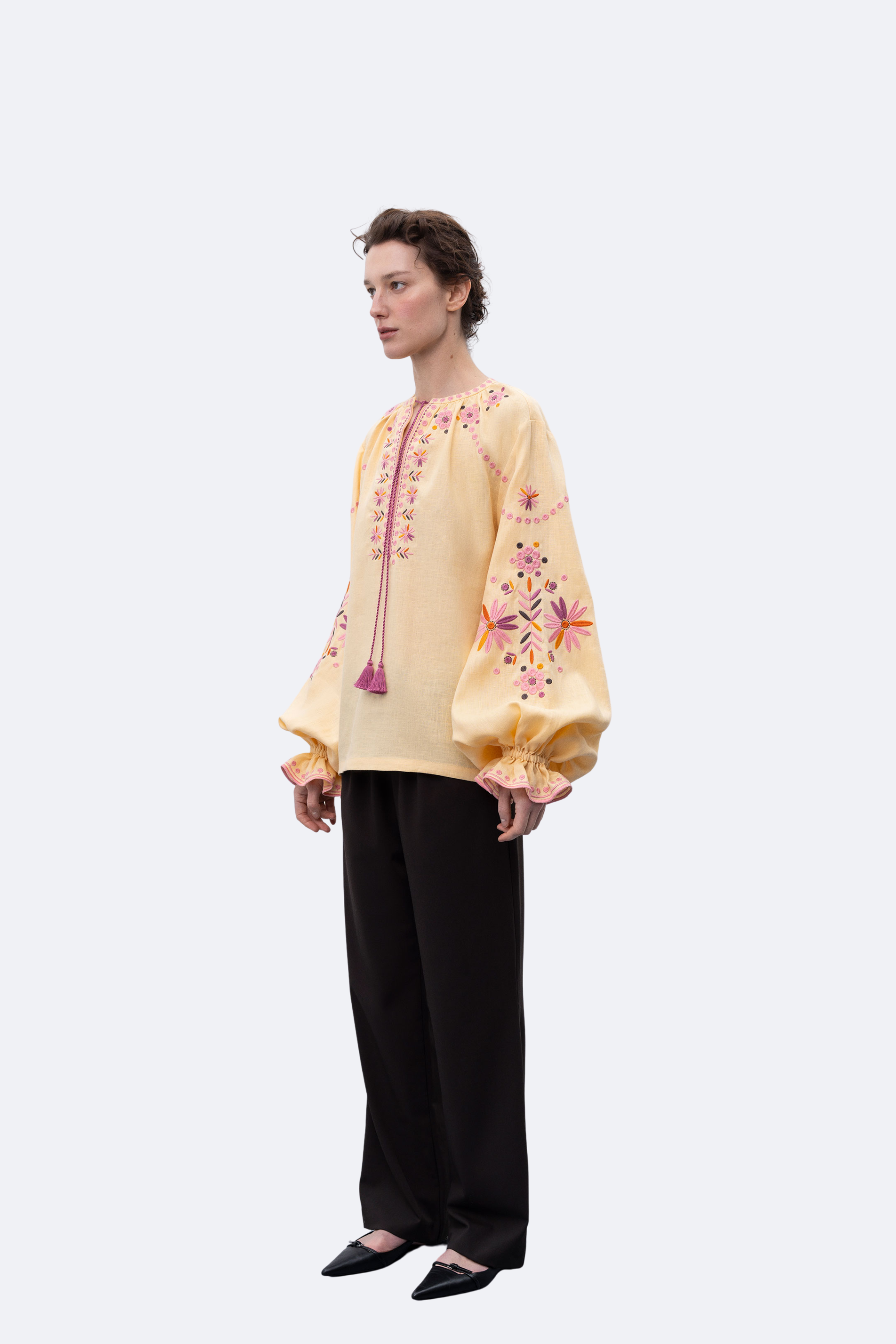 Woman wearing a yellow embroidered blouse and black pants on a white background