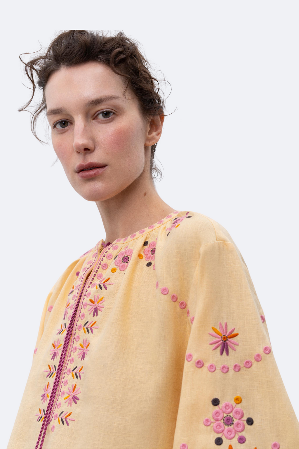 Woman wearing a yellow embroidered top with colorful patterns on a white background