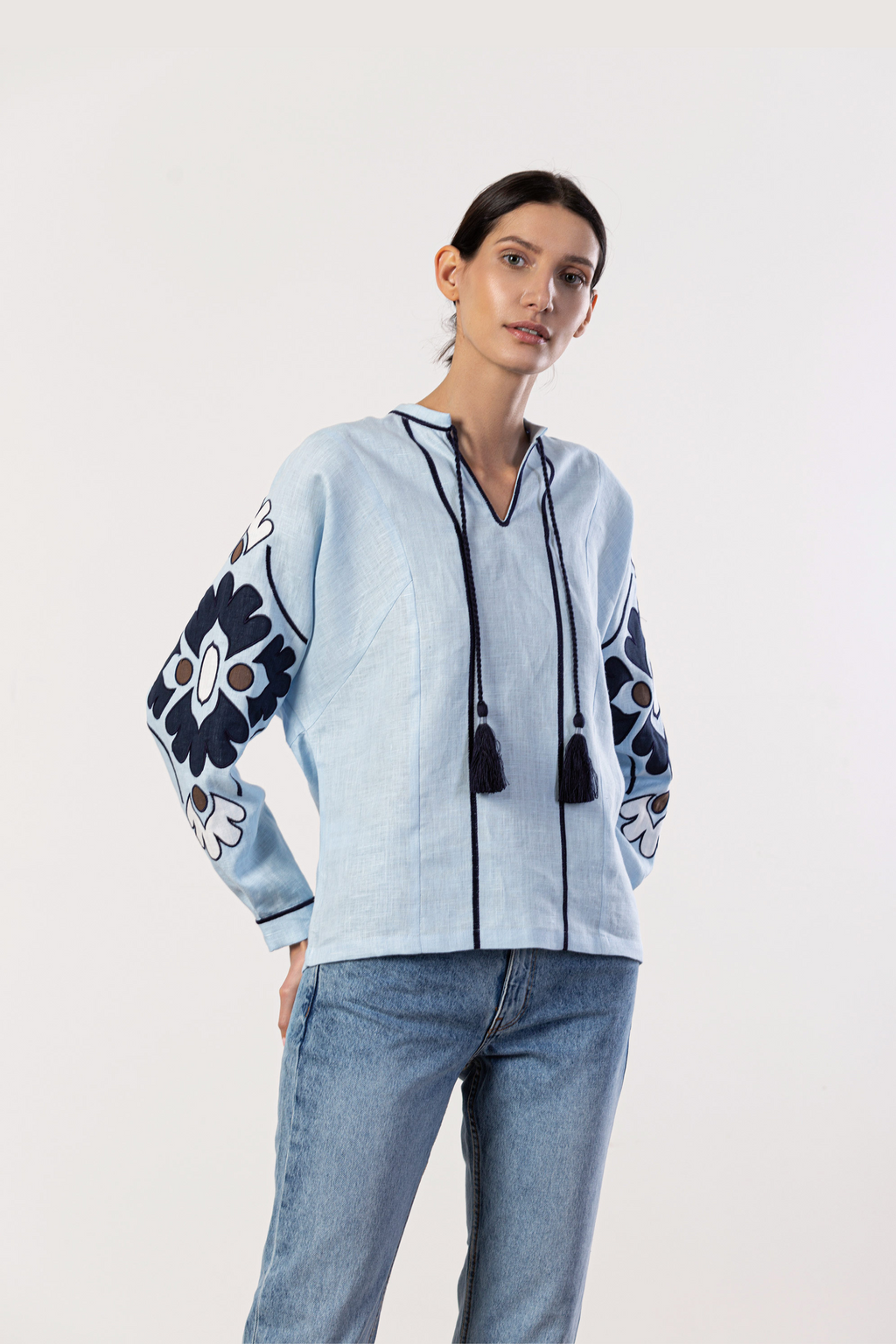 Woman wearing a light blue jacket with floral patterns and tassels on a white background