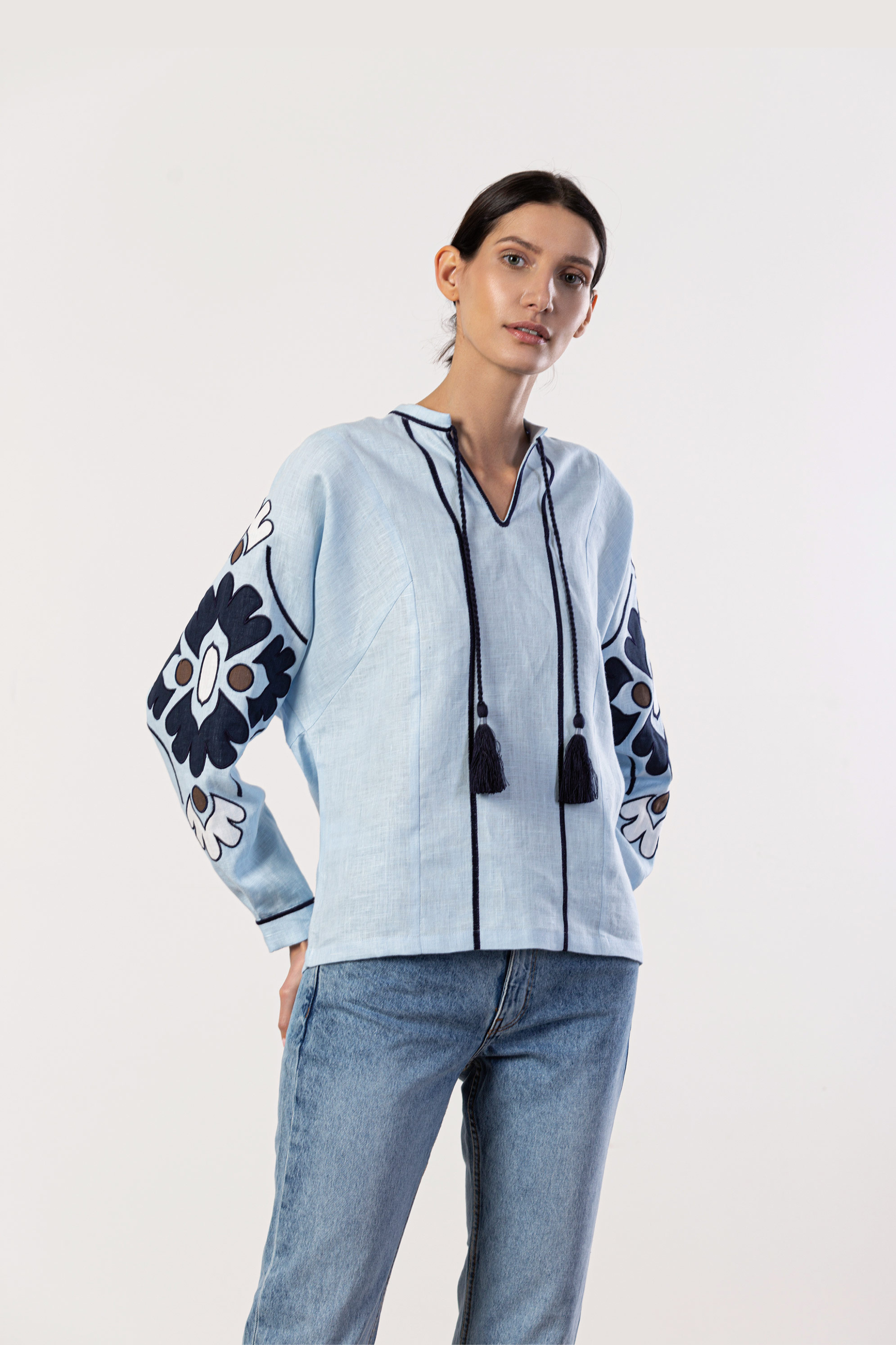 Woman wearing a light blue jacket with floral patterns and tassels on a white background