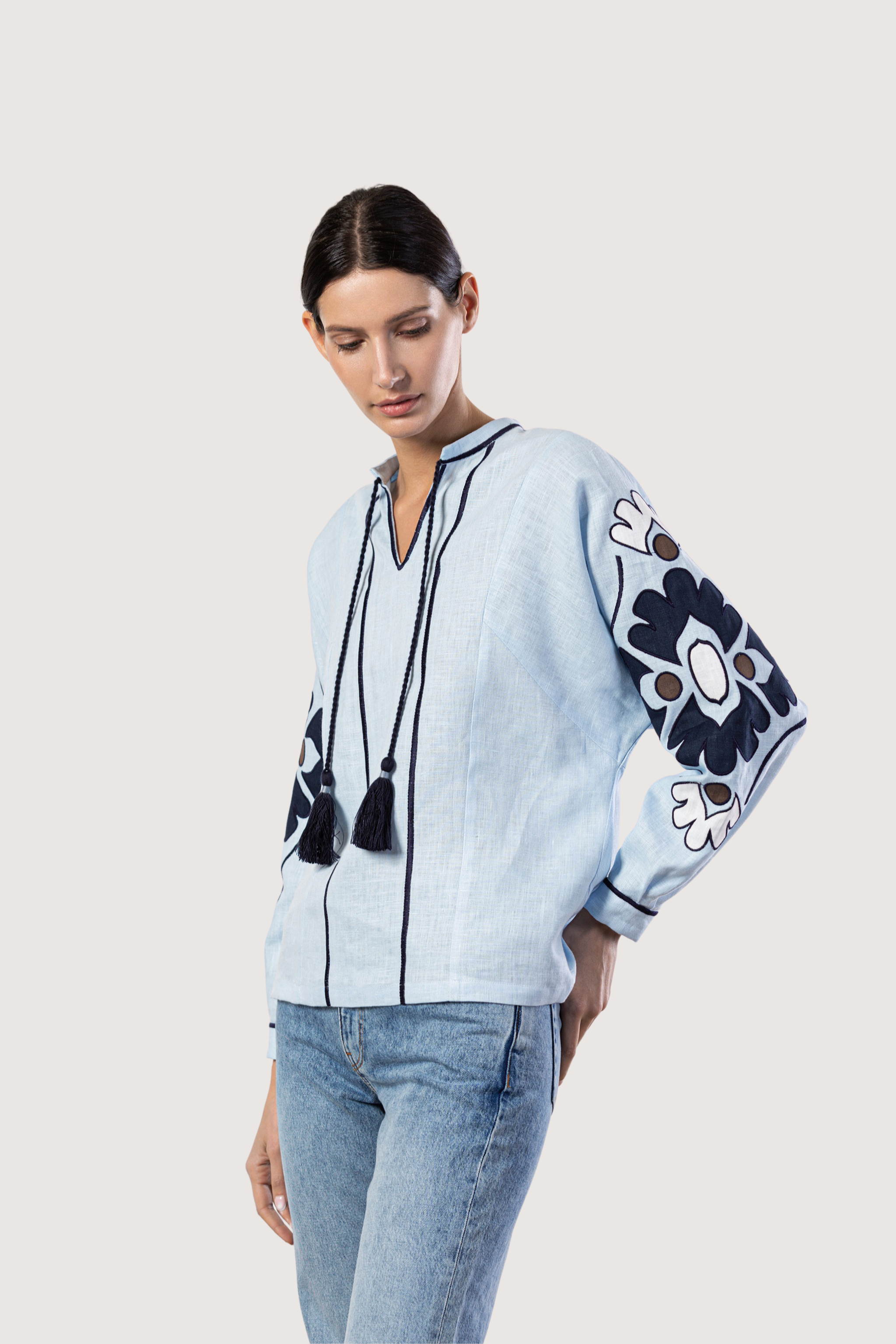 Woman wearing a light blue blouse with floral embroidery and jeans on a white background