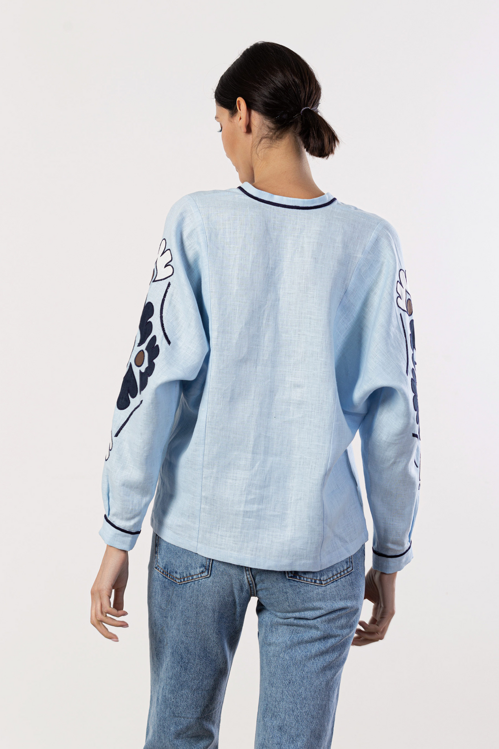 Person wearing a light blue sweatshirt with floral designs on sleeves against a white background