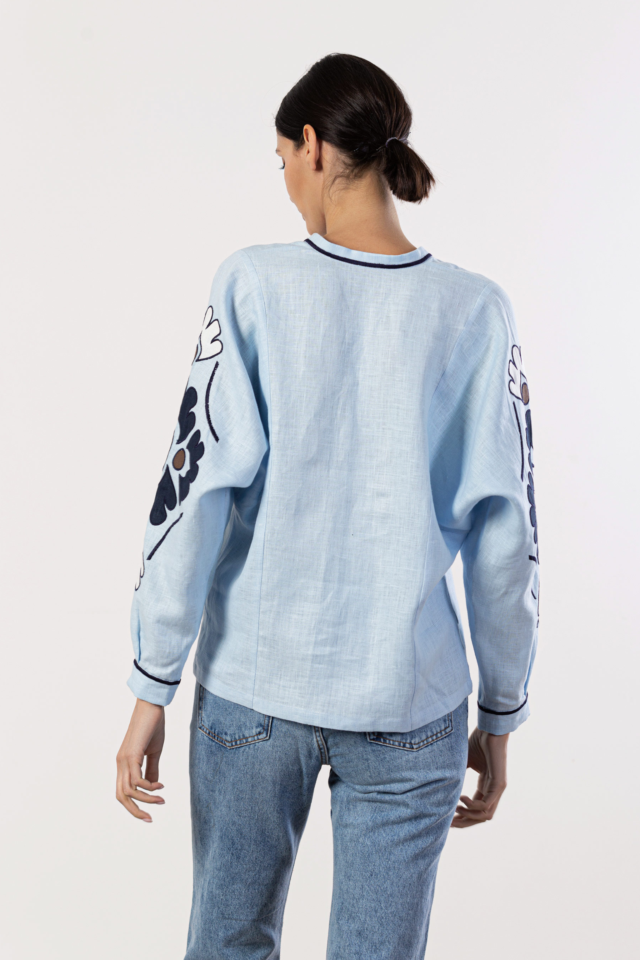 Person wearing a light blue sweatshirt with floral designs on sleeves against a white background