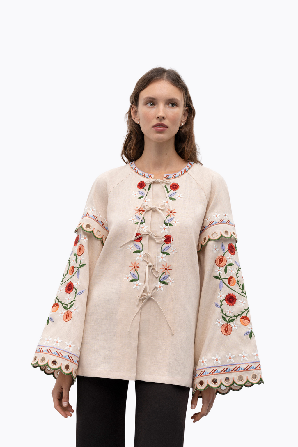 Woman wearing a cream blouse with floral embroidery on a white background