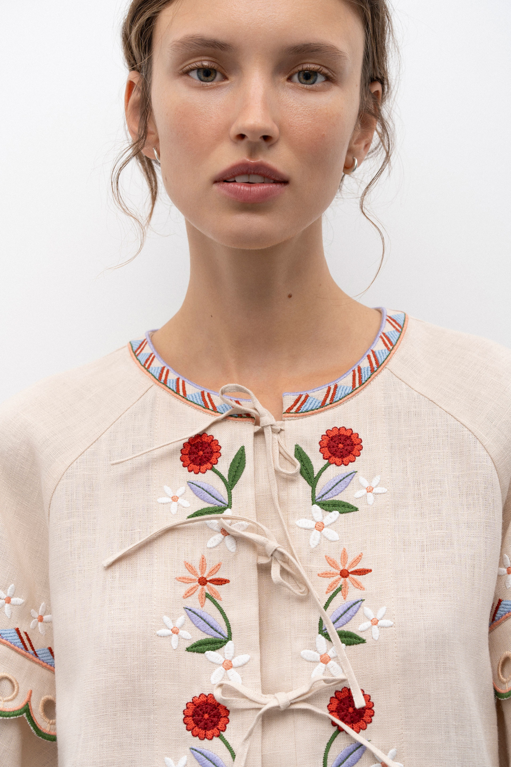 Woman wearing a cream-colored blouse with floral embroidery on a white background