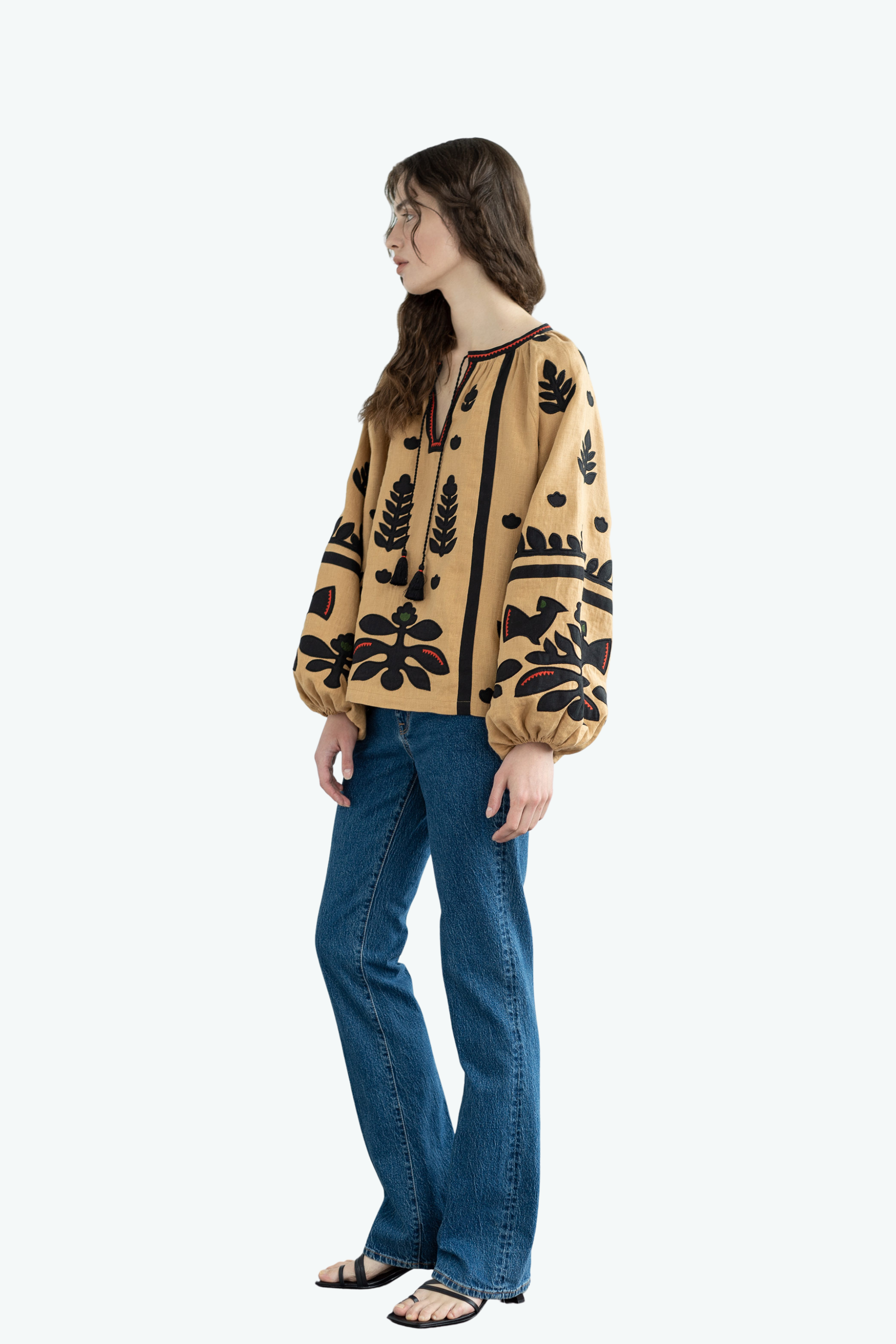 Woman wearing a patterned blouse and blue jeans on a white background