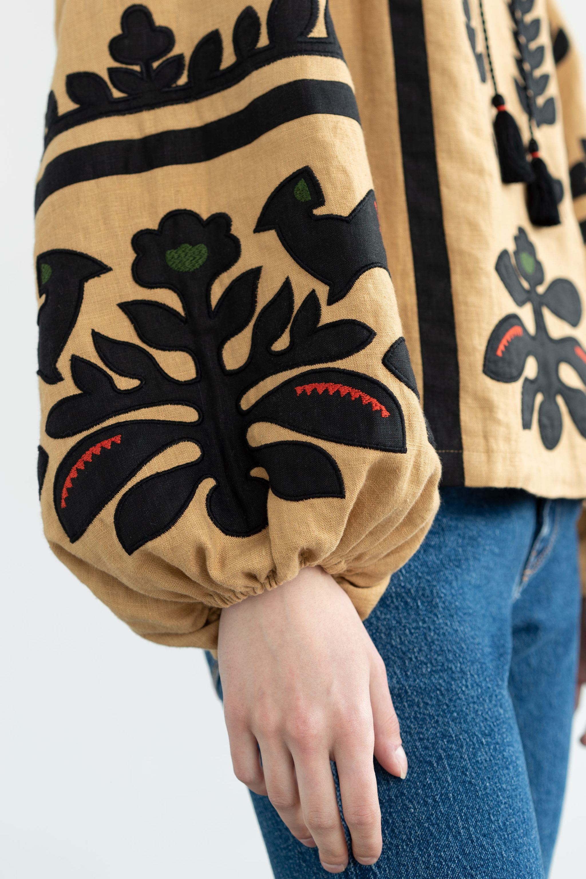 Close-up of a person wearing a beige jacket with black floral patterns on a white background