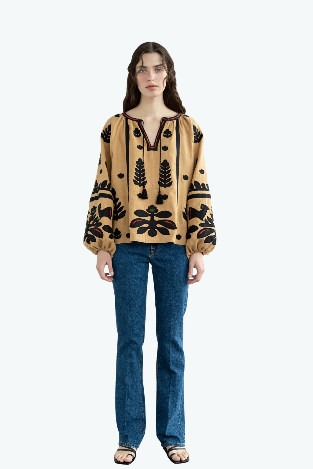 Woman wearing a beige blouse with black floral patterns and blue jeans on a white background