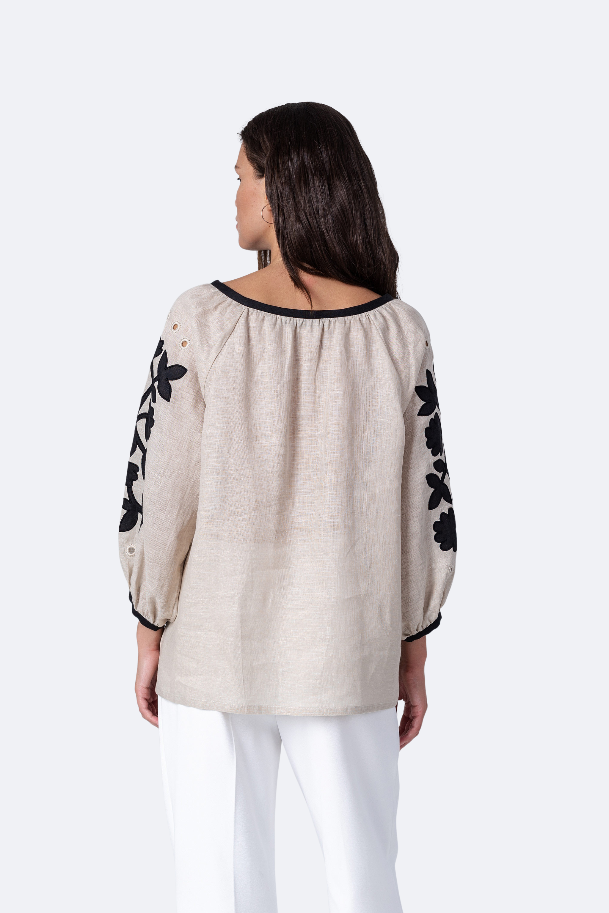 Woman wearing a beige blouse with black floral patterns on sleeves against a white background