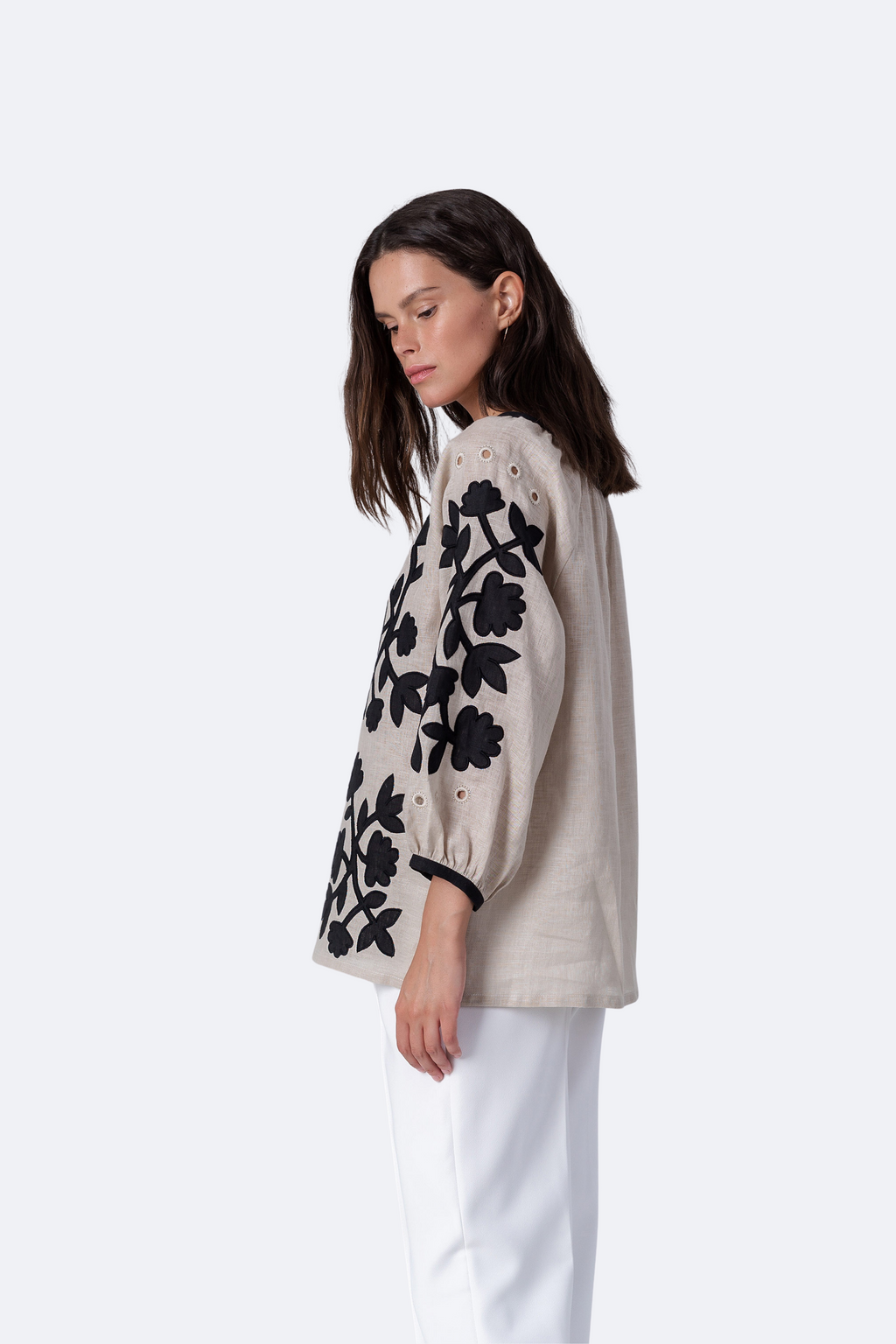 Woman wearing a beige sweater with black floral patterns on a white background