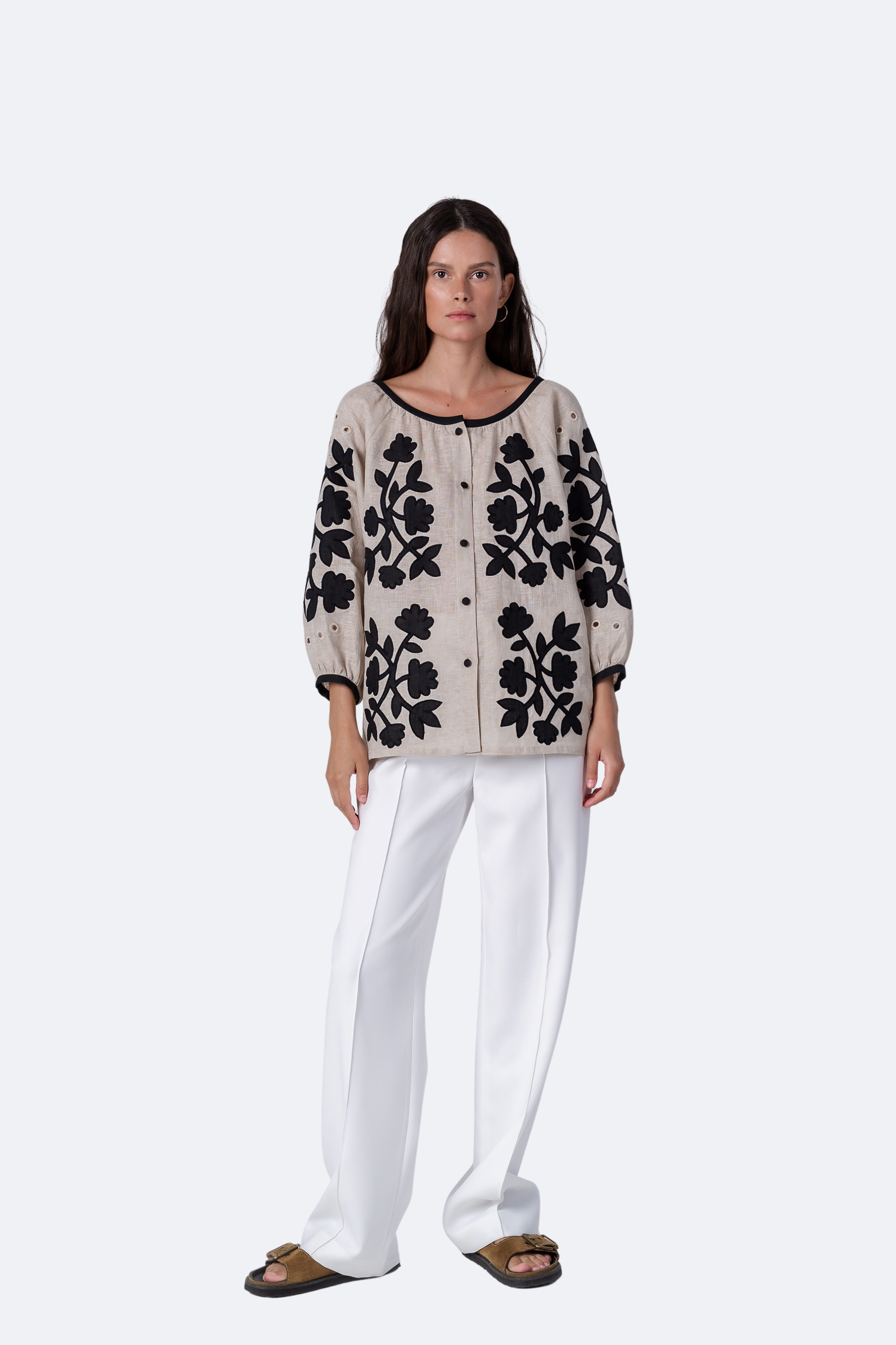Woman wearing a floral patterned cardigan and white pants on a white background