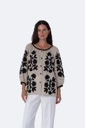 Woman wearing a beige blouse with black floral embroidery on a white background