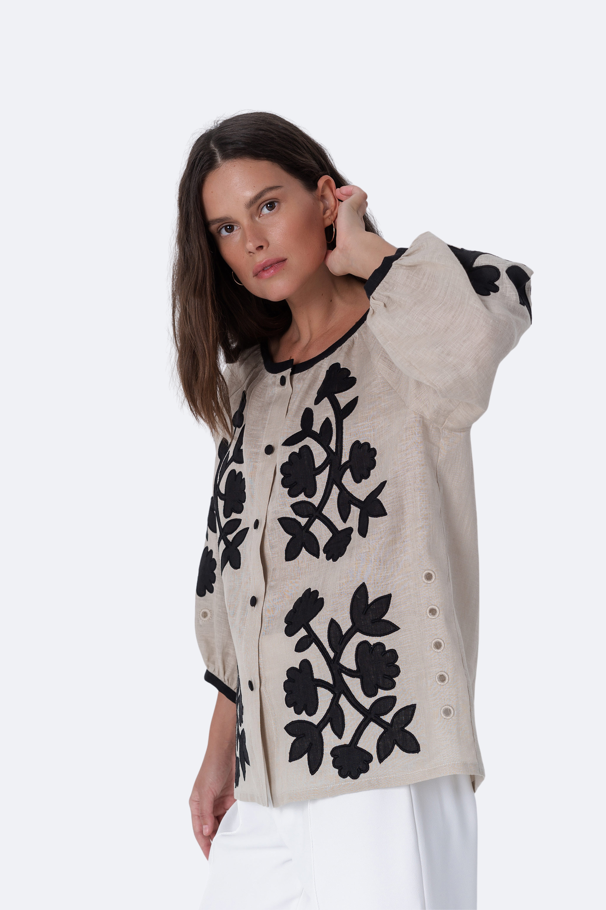 Woman wearing a beige sweater with black floral patterns on a white background