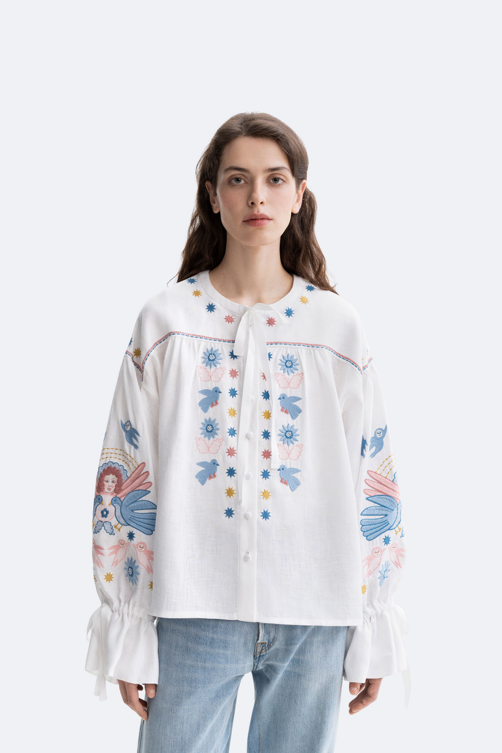 Woman wearing a white blouse with colorful floral embroidery on a white background