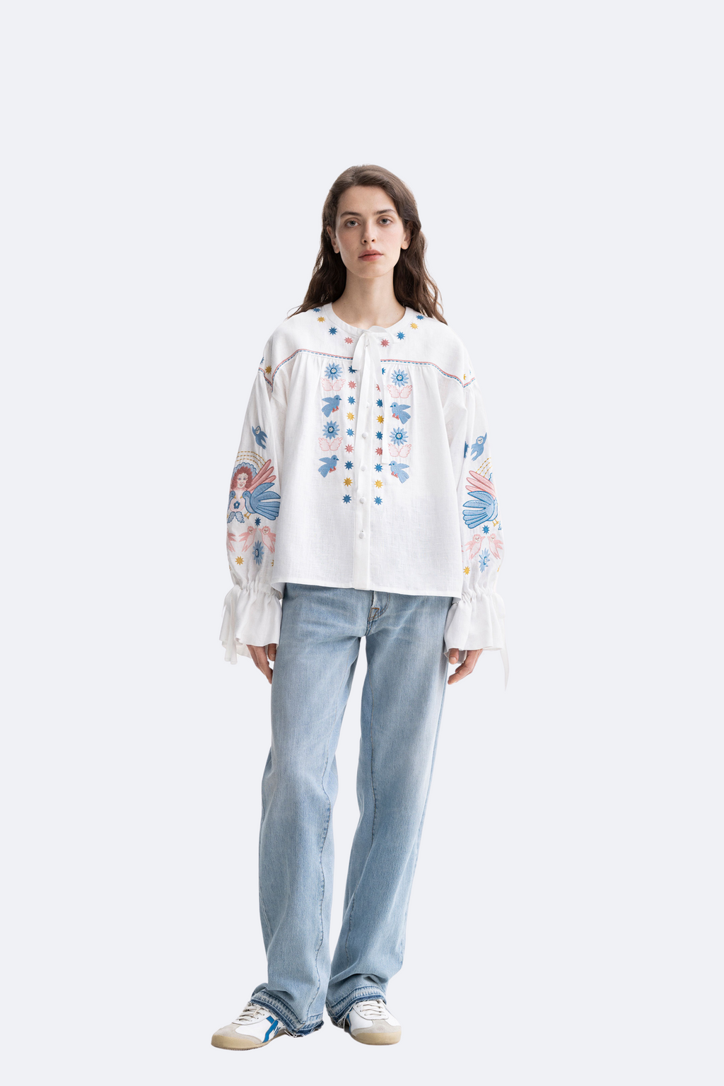 Woman wearing a white blouse with floral patterns and light blue jeans on a white background