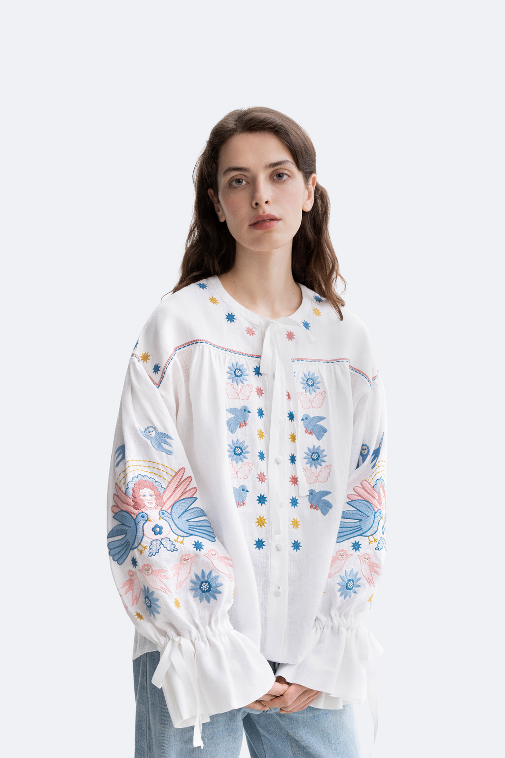 Woman wearing a white blouse with colorful floral embroidery on a white background