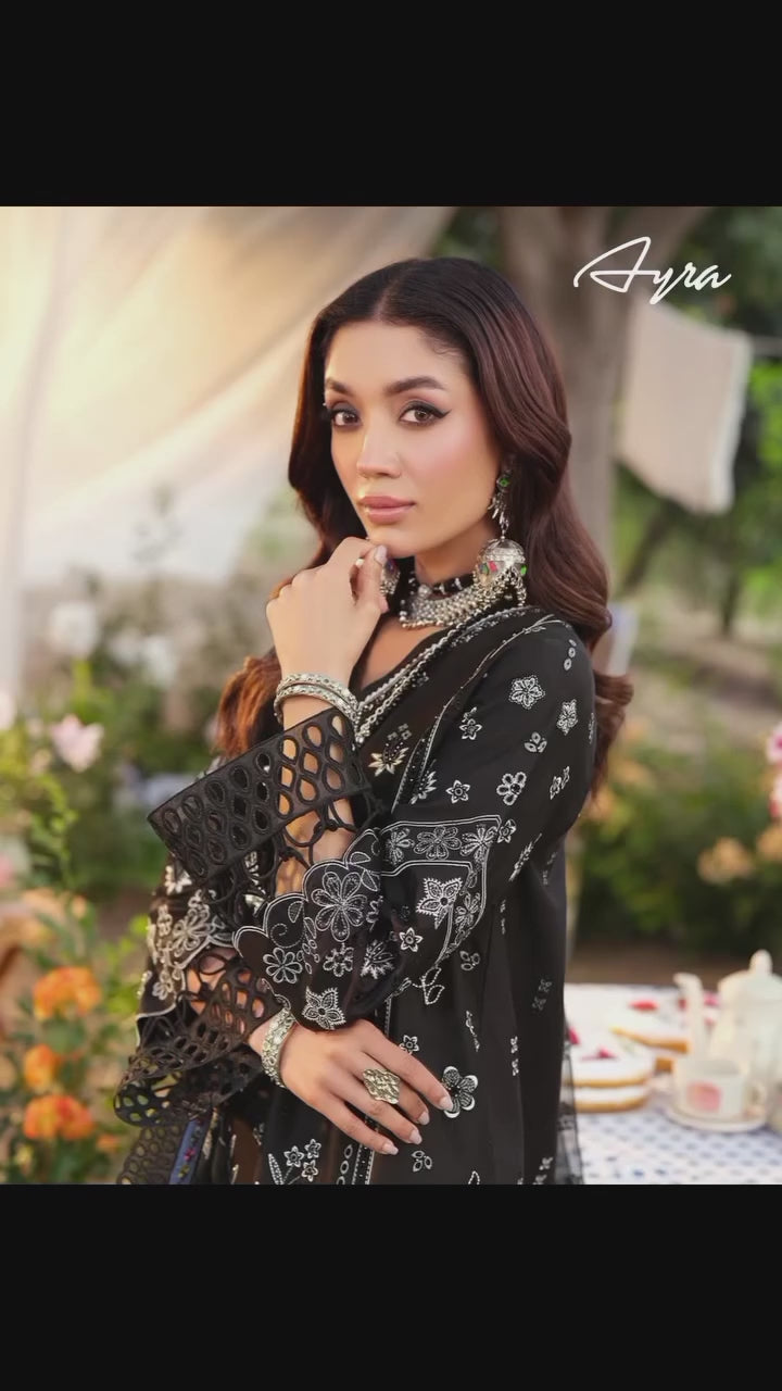 Woman in a black and white patterned dress standing behind a white picket fence in a garden setting.