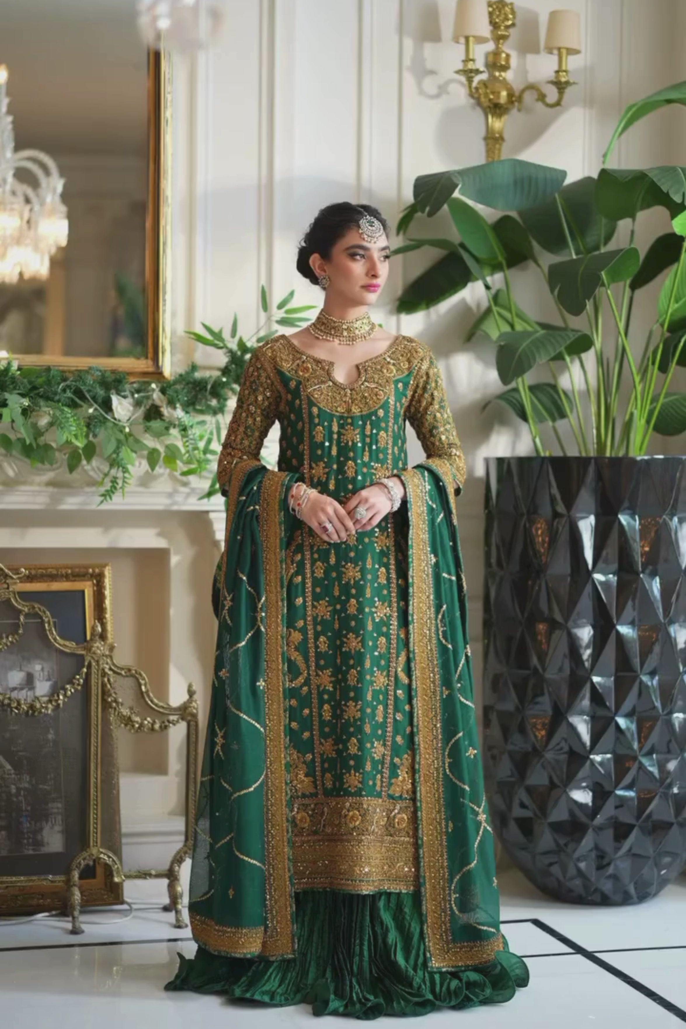 Woman in a green and gold dress standing in an elegant room with chandeliers and decorative elements.
