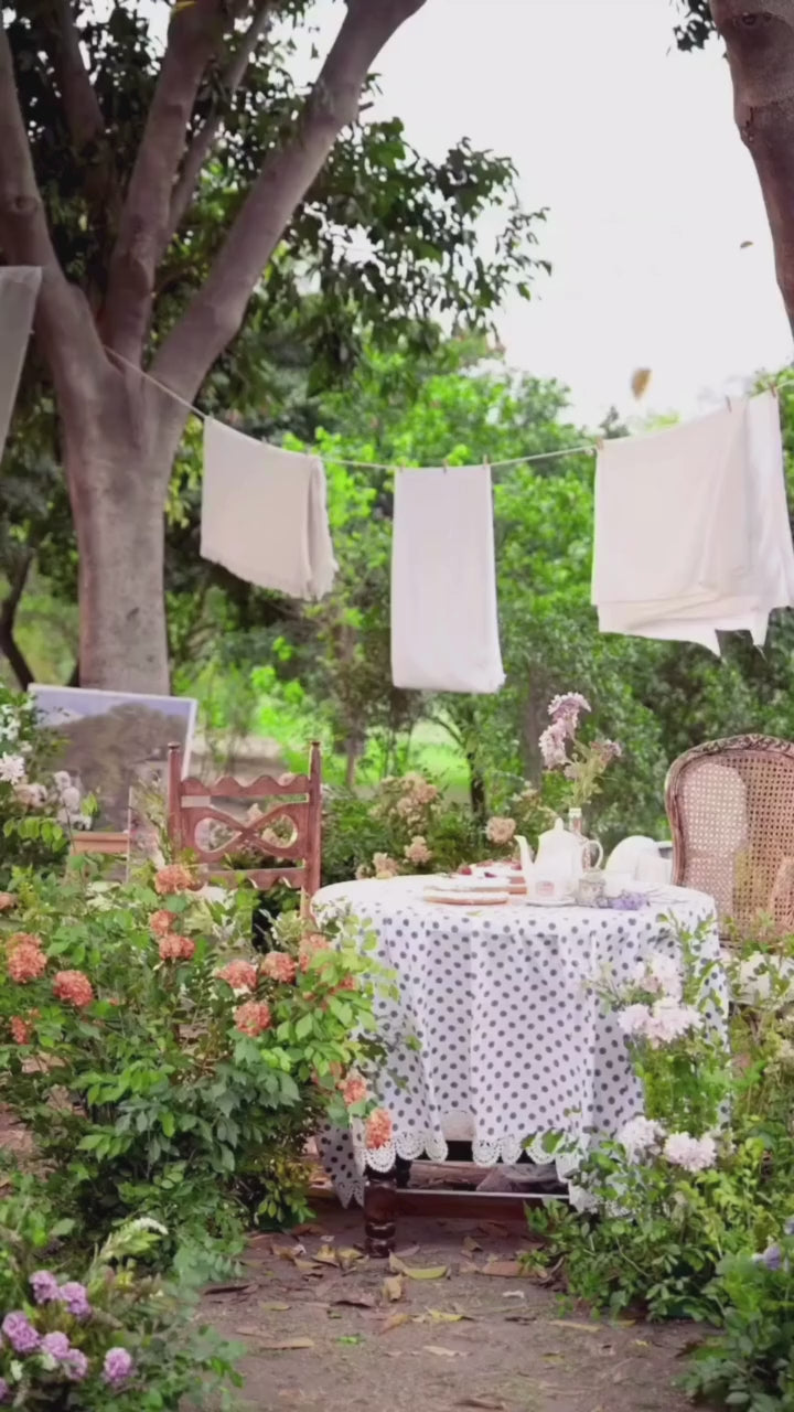 Woman in black embroidered outfit standing outdoors with floral decorations and tables.