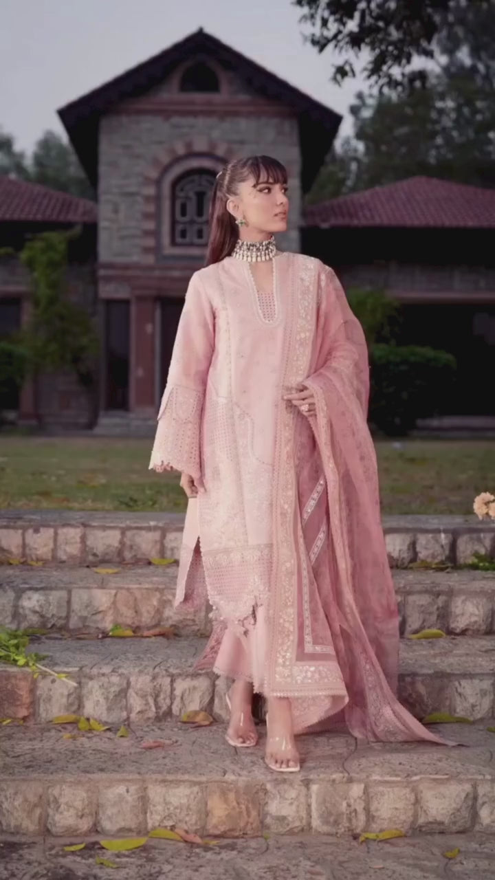 Woman in a pink traditional outfit standing on stone steps with greenery in the background
