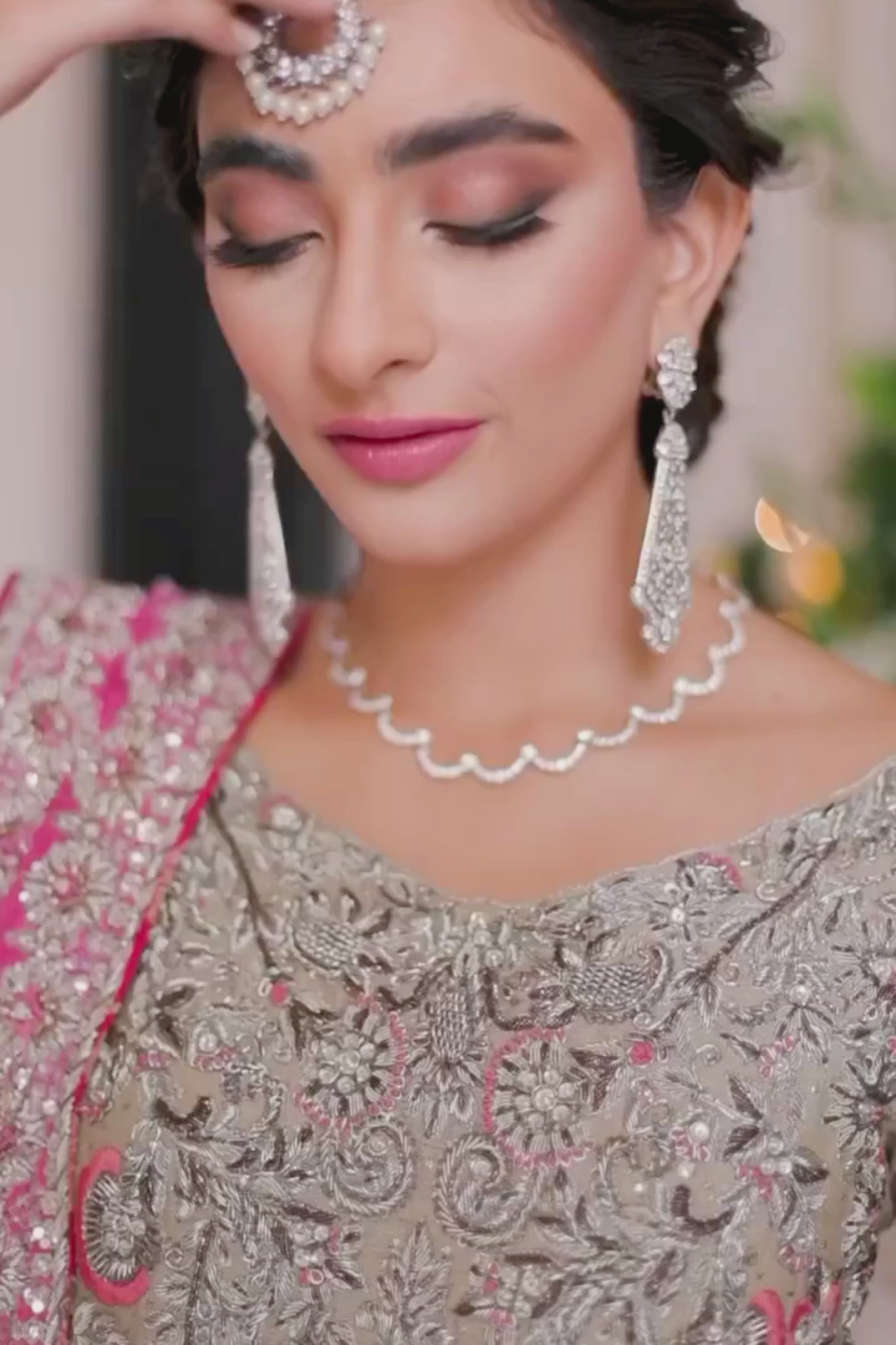 Woman in a traditional outfit with a pink dupatta standing in a decorated room.