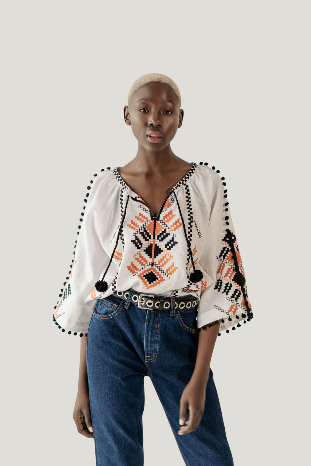 Woman wearing a patterned blouse with bell sleeves and blue jeans on a plain background