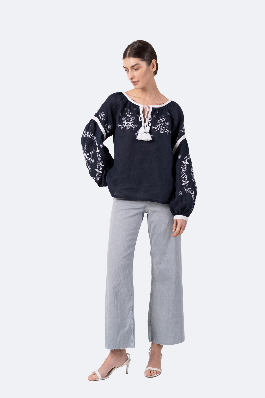 Woman wearing a black embroidered blouse and gray pants on a white background